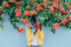 Black woman in yellow coat poses under a blossoming bush.