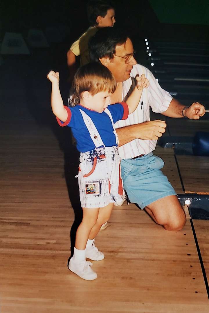 Uncle bowling with little nephew wearing suspenders.