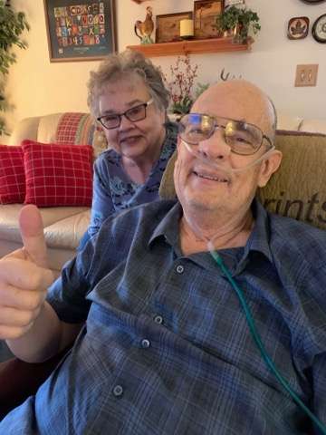 Dan reclining and holding a thumbs up next to his sister.