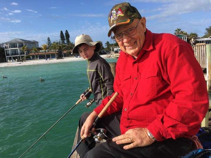 Dan Hopkins in red shirt fishing on a pier with grandosn.
