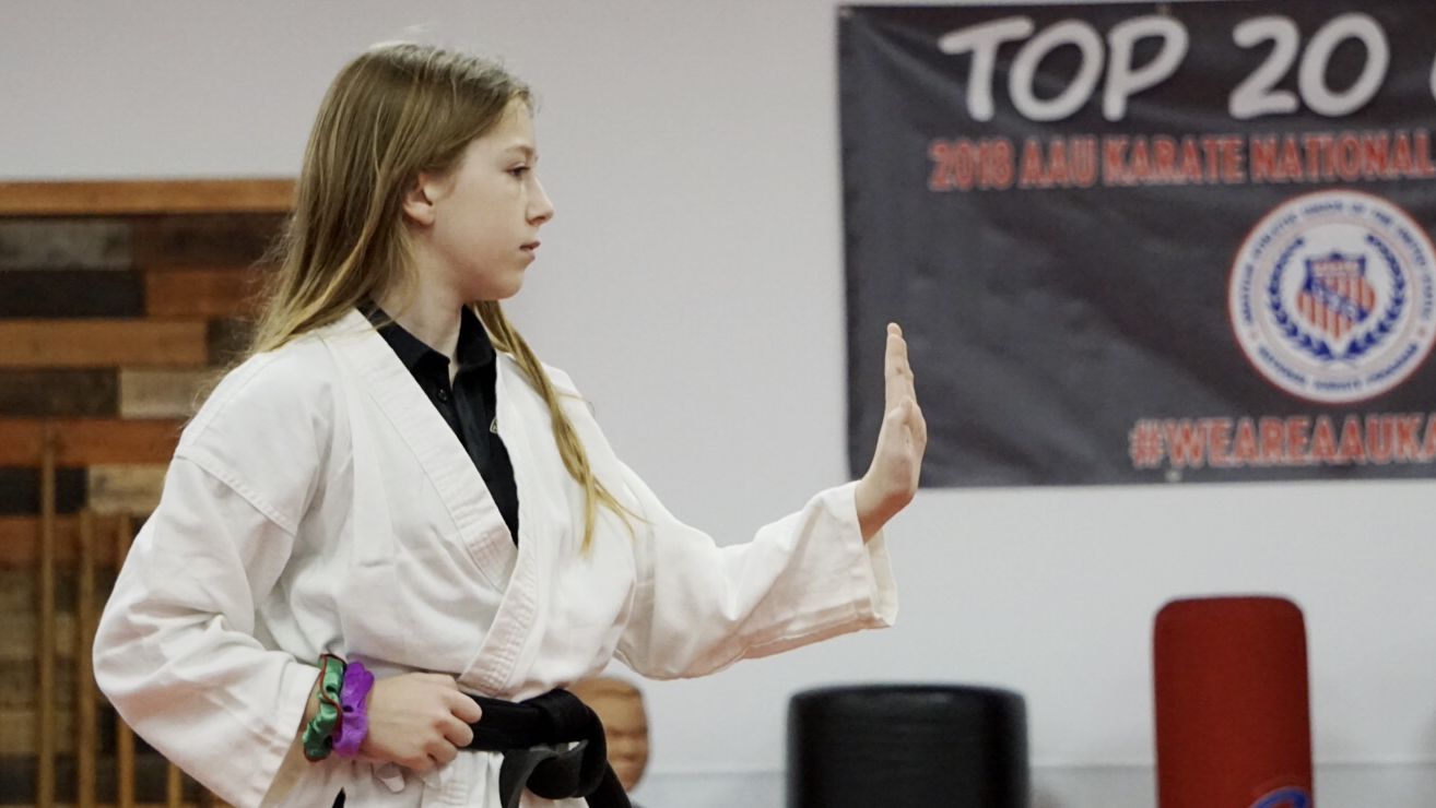 Female karate student practices kata, arm extended with hand up-turned.
