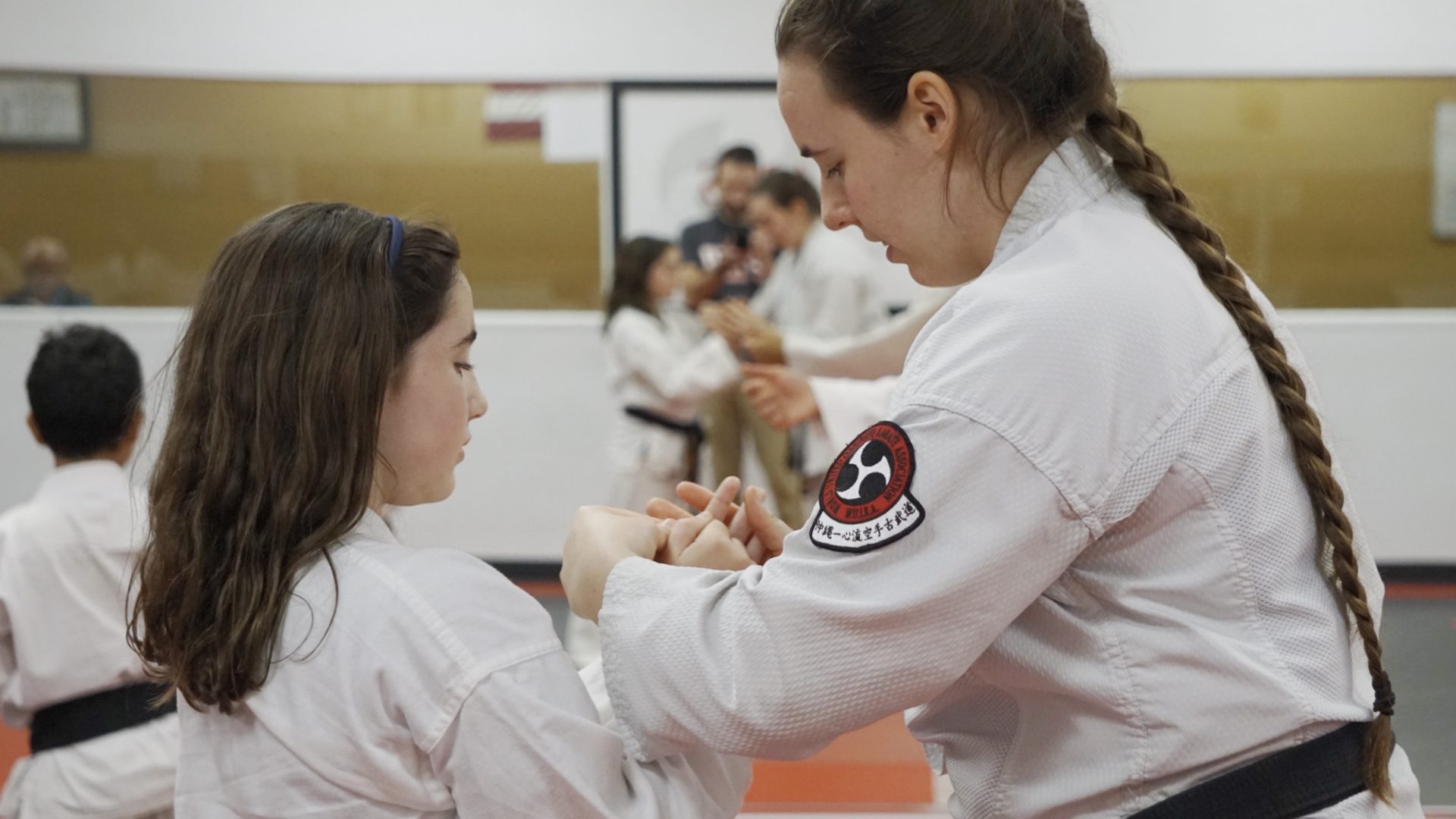 Teen sensei helps a female student with hand position during kata.