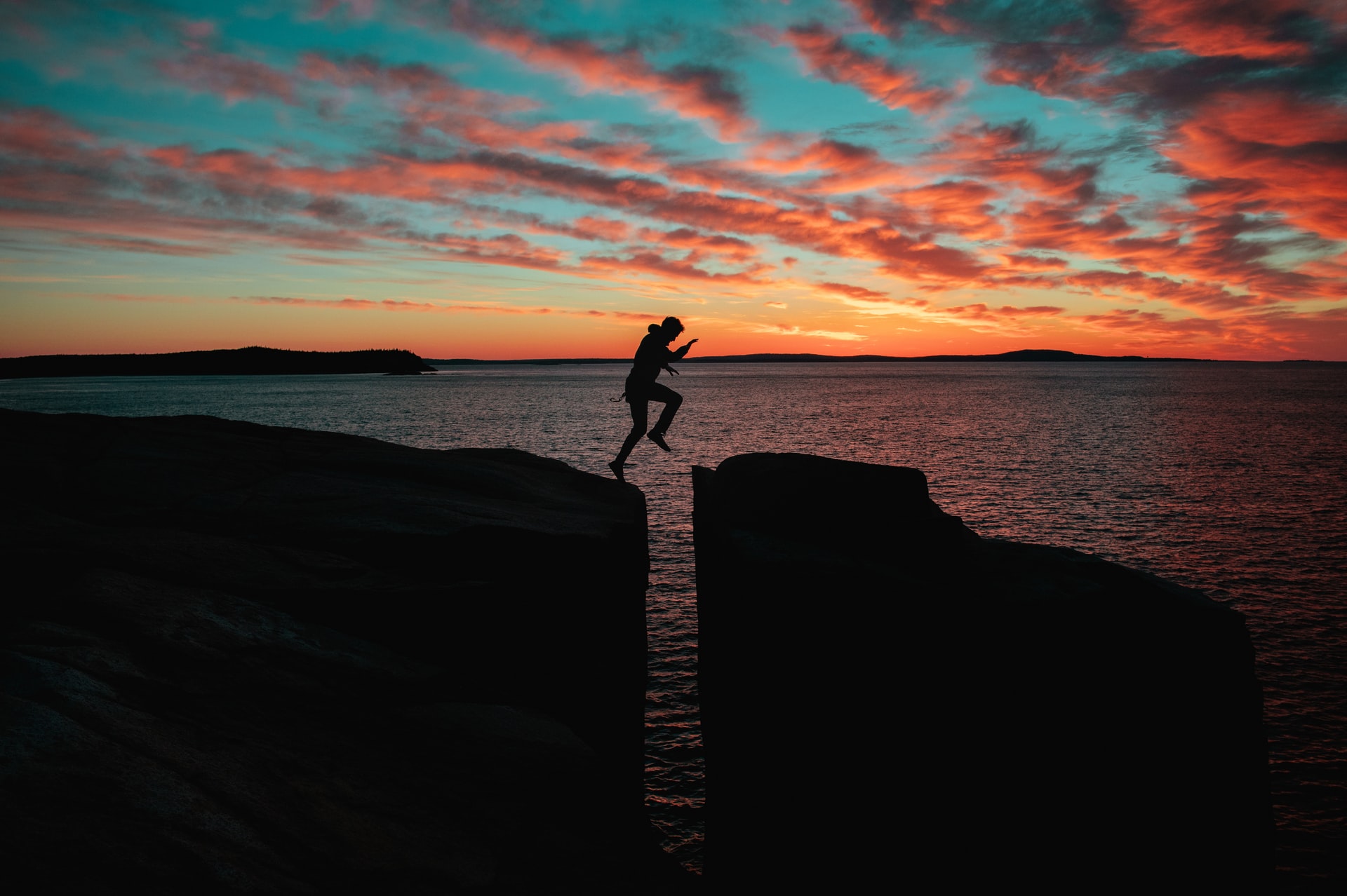 Silhouetted man hopping over a crevice at sunset.